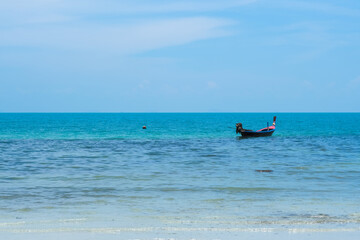 A tranquil beach scene featuring fishing boats resting on soft white sand, the clear blue sea stretching to the horizon, and a sunny sky.