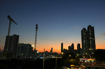 Fototapeta premium Dec 16 2024,Hong Kong.A series of construction cranes rise against a colorful sunset, casting long shadows over a busy construction site