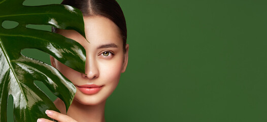 Close up woman face with green exotic leaf. Skin care beauty treatments concept. Model with clean, health skin of face. Monstera Leaves