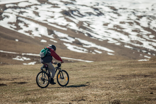 Cyclist riding on a mountain path with snow patches in the backg