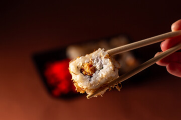 Chopsticks taking portion of sushi roll. Sushi rolls with salmon cream cheese and cucumber in take away package. Food delivery concept.