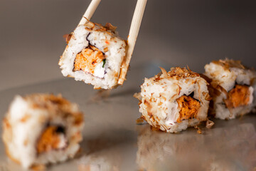 Chopsticks taking portion of sushi roll. Sushi rolls with salmon cream cheese and cucumber. Isolated. Sushi roll on grey background.