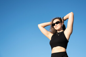 Summer portrait against blue sky of young Asian woman young in black clothes and sunglasses.