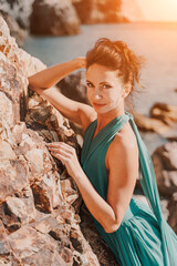 Woman green dress sea. Woman in a long mint dress posing on a beach with rocks on sunny day. Girl on the nature on blue sky background.