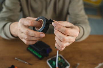 Person applying black tape to wires on a wooden table surface.