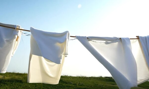 Freshly washed linens hanging on a clothesline under a clear sky.