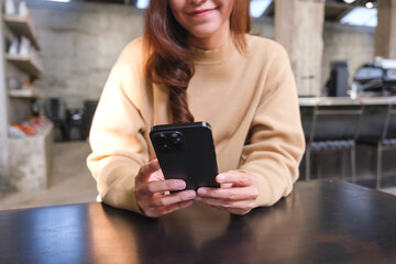 Closeup image of a young woman holding and using mobile phone in cafe