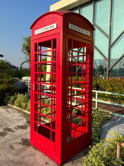 Classic red telephone booth in garden setting.