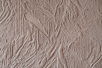 Wall surface with textured paper wallpaper of beige color, photographed at an angle. An example of how dust accumulates on such surfaces in the house, the need for cleaning