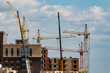 Building under construction with cranes against the background of a cloudy sky.