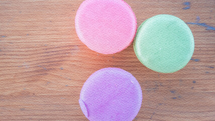 Three small, colorful, and possibly textured objects sit on a wooden surface