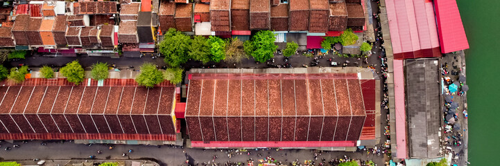 Aerial view of a bustling Asian market with vibrant red roofs and greenery, illustrating urban...
