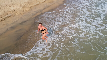 A woman in a black bikini runs along the shoreline, embodying summer fun and beach relaxation