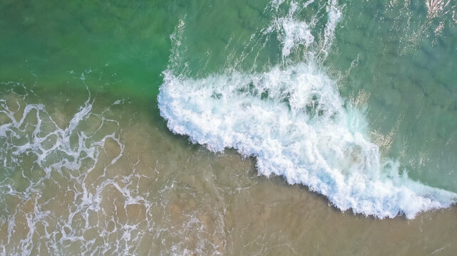 Aerial view of ocean waves crashing onto a sandy beach, symbolizing summer vacations and relaxation by the sea