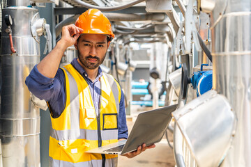 Asian male technical foreman in safety uniform inspects maintenance work work holding a laptop to look at plumbing and electrical systems on the roof of a building, Industrial background