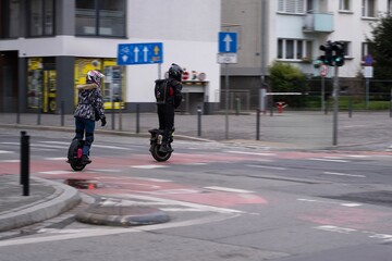 Two people riding electric unicycles across a city street, wearing helmets and protective gear © Nataliia
