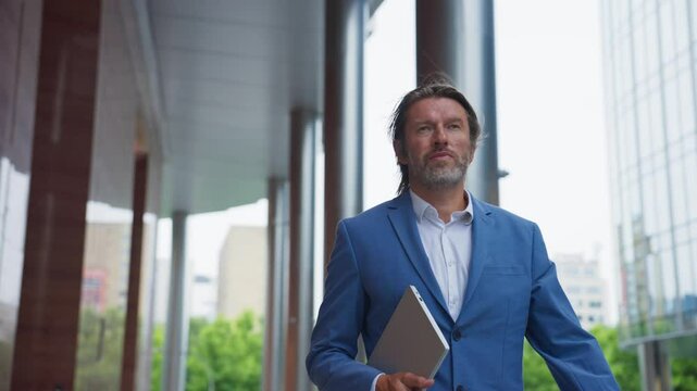 Focused Caucasian male looking straight ahead and confidently walking. Carrying small laptop. Stylish outfit. Businessman going to meeting. Prepared for upcoming company expansion.