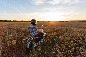 Biker girl in a rye field against the backdrop of sunset