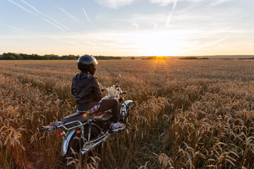 Biker girl in a rye field against the backdrop of sunset