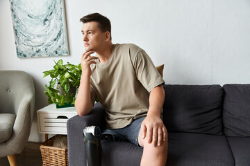 Handsome young man sits on couch, deep in thought, showcasing his prosthetic leg in a stylish space.