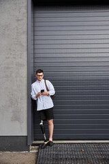 Handsome young man with a prosthetic leg stands casually while using his phone.