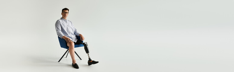 A young handsome man sits relaxed in a chair, showcasing his prosthetic leg with pride in a studio.