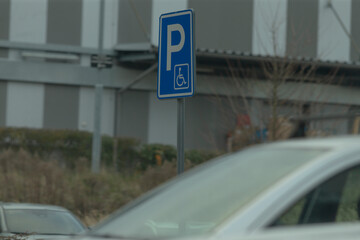 A car, which appears to be an everyday family vehicle, is parked directly in front of a prominent handicapped parking sign