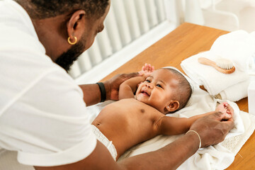 A joyful father interacts with his smiling baby during a tender moment on a changing table,...