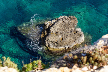 a dangerous view from above the cliffs into the clear water of the coastline of Comino, Malta. With...