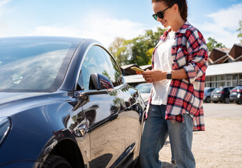Woman unlocking car-sharing auto remotely with mobile app and smartphone on city street.