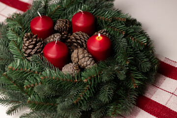 Close up of an advent wreath with one red burning candle on white table 