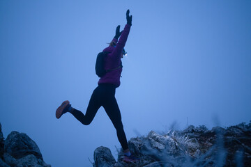 silhouette of a fitness woman trail runner jumping over a cliff and running to a rocky mountain top