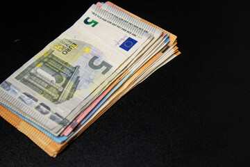 Close up of a stack five, ten, twenty and fifty euro bills, black background 
