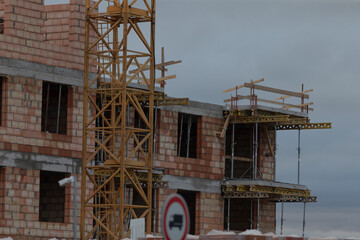 A brick building is currently under construction, and prominently in the foreground is a large crane facilitating this process