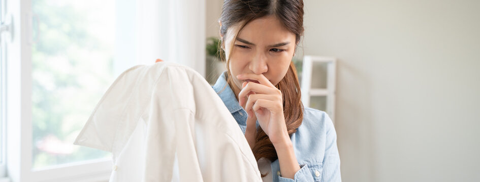 Smelly clothes laundry, housewife woman having bad smelling clothes on the hand holding breath nose with finger, sniff smelly dirty stinky musty and look disgusting.