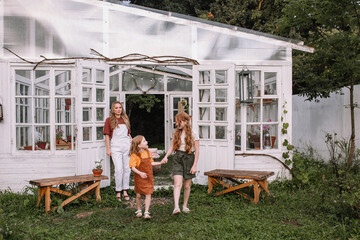 Woman mother and two red-haired daughter girls care and plant plants in pots in a greenhouse, doing gardening in the spring for Earth Day.