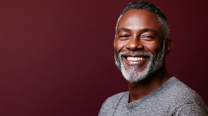 Smiling mature man with grey beard against maroon backdrop