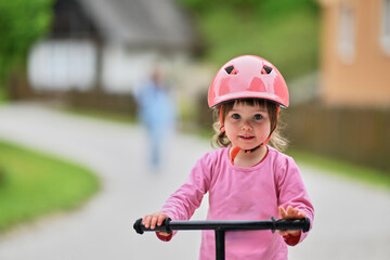 A little girl, dressed in a cute outfit and wearing a helmet, excitedly learning to ride her bike for the first time, filled with joy and determination.