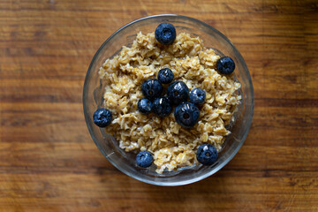 Oatmeal porridge in bowl with blueberries on a wooden table background, healthy breakfast food. Top view.