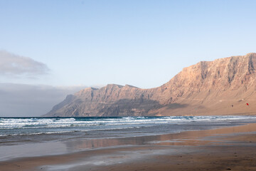 Waves gently crash on a sandy beach with cliffs in the background at sunset