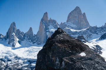 Obraz premium A breathtaking view of the Fitz Roy mountain range in Patagonia, Argentina, captured on a clear day. The sharp granite peaks rise dramatically against the deep blue sky, This iconic landscape