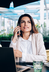 Beautiful caucasian female in smart casual wear having mobile phone conversation while working remotely on cafe terrace, 30s pretty confident business woman making call in roaming discussing plans