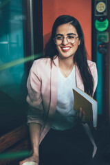 Happy Hispanic female student in eyewear for vision protection resting at sidewalk spending leisure...