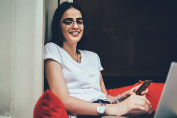 Portrait of pretty female copywriter in eye spectacles smiling at camera while doing remote job on...