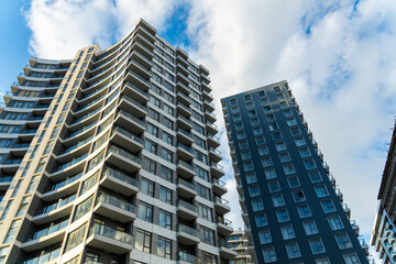 Fototapeta premium Modern apartment buildings with glass balconies standing tall under a blue sky with white clouds, showcasing contemporary urban architecture
