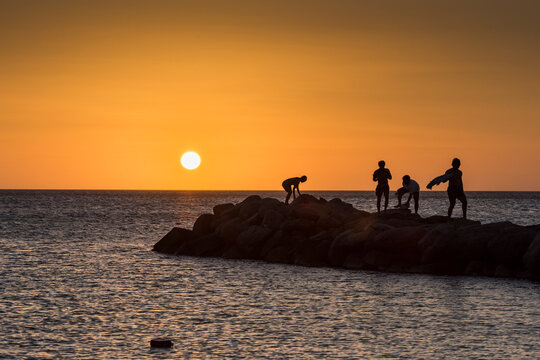 Group of youths enjoy a peaceful sunset moment on a rocky outcrop on a beach in Noord, along the coast of Aruba - Powered by Adobe