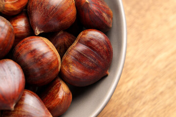 Fresh organic chestnuts with smooth brown shells in ceramic bowl. Close-up view on a wooden background