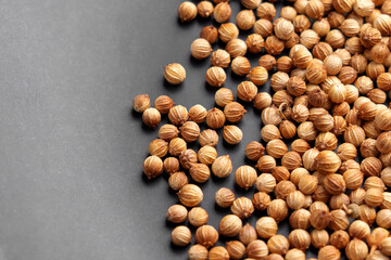Dried coriander seeds with textured brown shells scattered on a dark surface. Aromatic spice