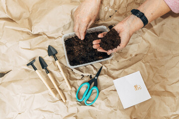 Kraft paper background, fertile soil and garden tools, top view. Hands planting seeds