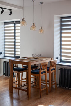 Contrast modern kitchen interior with horizontal blinds on windows, zebra shades. Wooden high bar table and chairs at dining space. Vertical image.